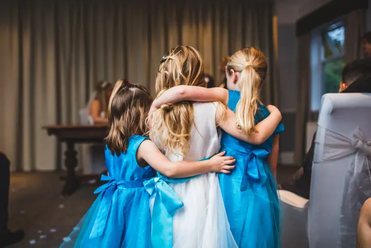 Bride hugging two flower girls in bright blue dresses after the ceremony