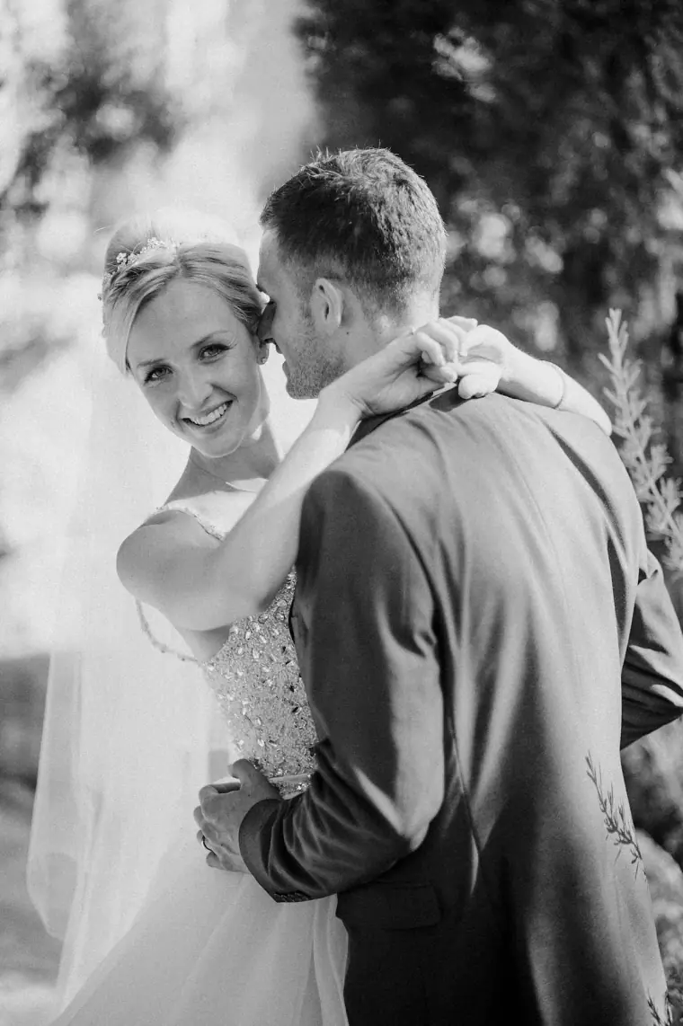 Black-and-white photo of the bride laughing as the groom hugs her