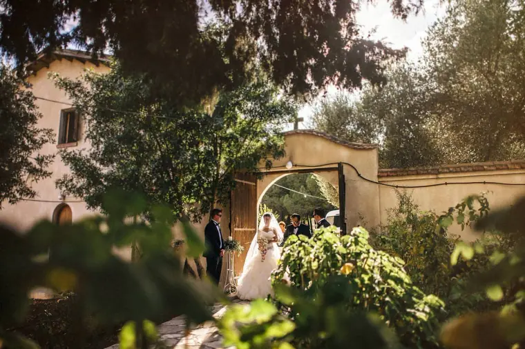 Bride entering through the stone gateway with her father, framed by greenery