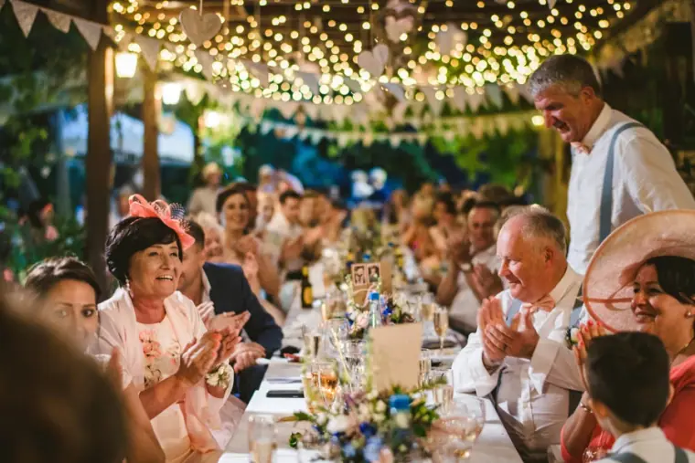 Guests clapping at long tables under festoon lights during the speeches