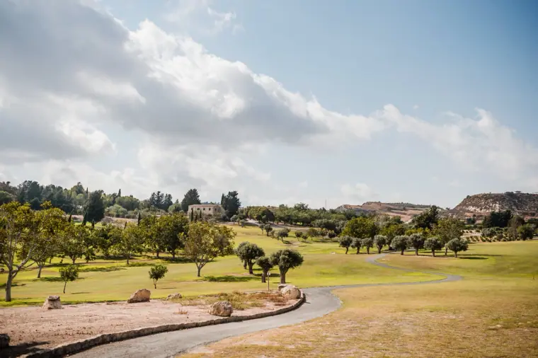 Rolling green golf course and olive trees at Minthis Hills under summer clouds