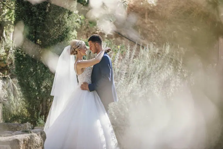 Bride and groom embracing among soft, sunlit greenery