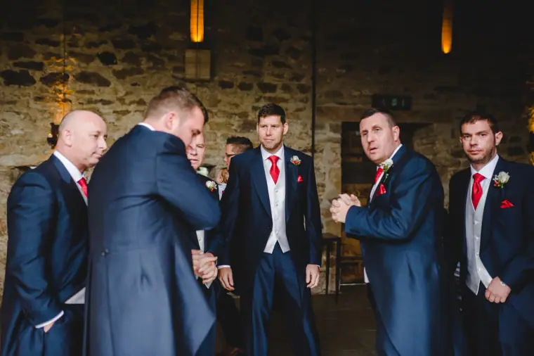 Groom and groomsmen in navy suits and red ties waiting in the barn