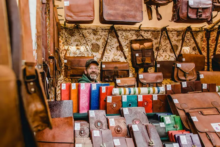Smiling stallholder surrounded by leather bags and journals at an Edinburgh market stall