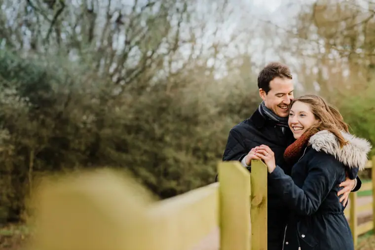 Couple smiling together as they lean on a wooden gate