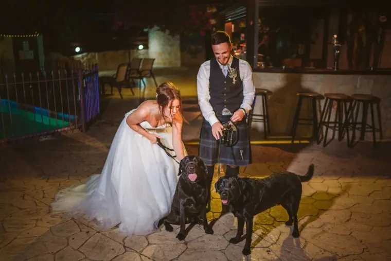 Hannah and Keith posing with two black Labradors on a lit terrace