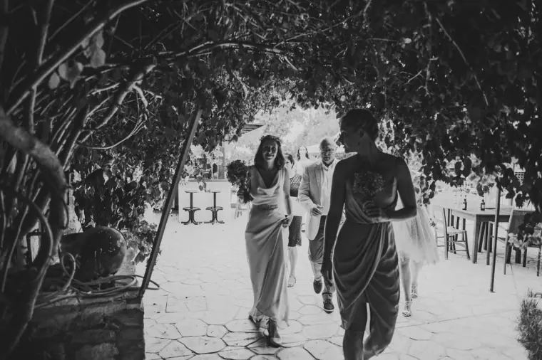 Black-and-white photo of the bride walking with her father beneath a vine canopy