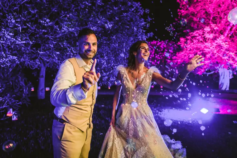 Groom pointing and smiling with his bride under pink and purple lighting