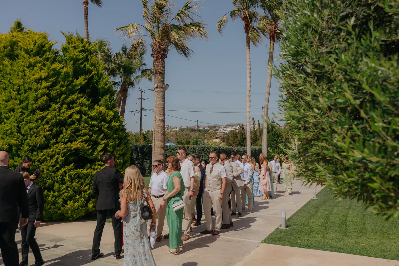Long line of guests making their way to the ceremony between palm trees