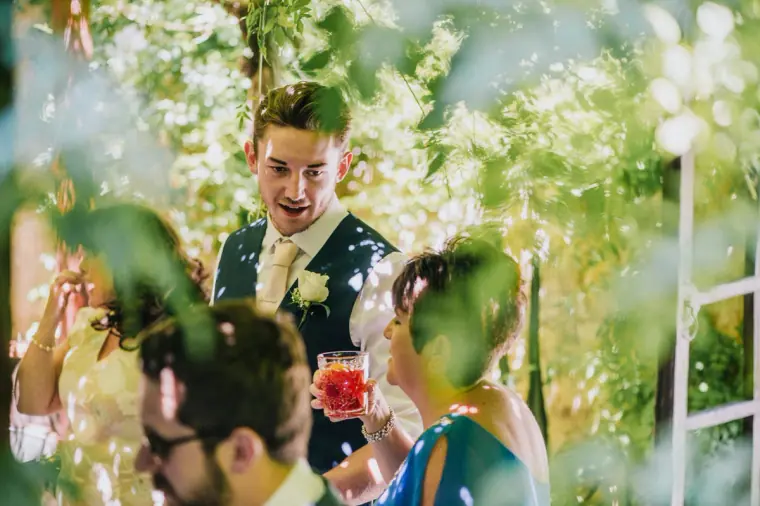 Smiling groomsman holding a drink among guests in the garden