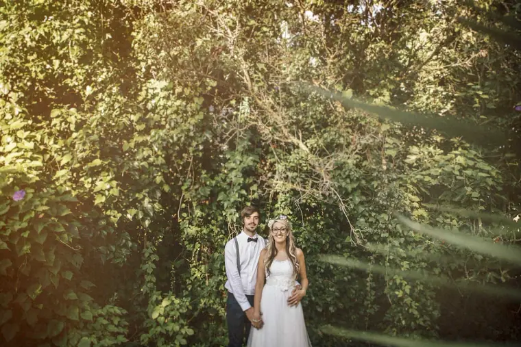Bride and groom standing together against a wall of green foliage