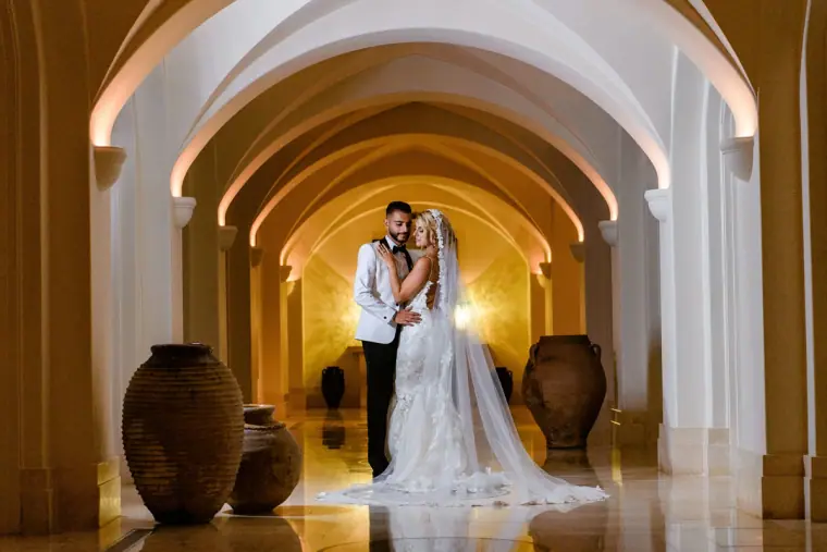 Couple standing in a candlelit arched corridor lined with large urns