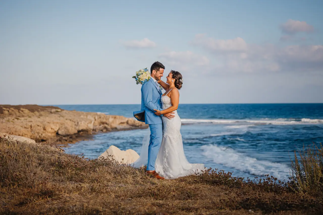 Bride and groom embracing on a rocky shoreline as waves break behind them