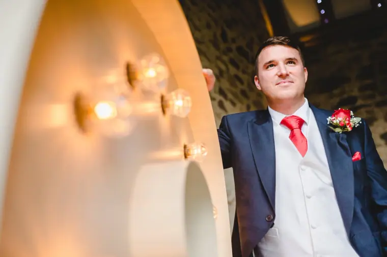 Groom in a navy suit and red tie smiling as he waits for the ceremony