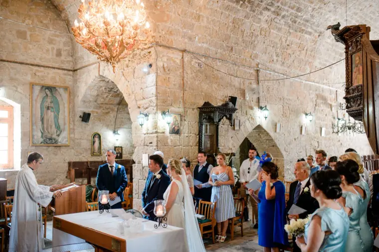 Priest conducting the ceremony before the couple and guests inside Ayia Kyriaki, Paphos