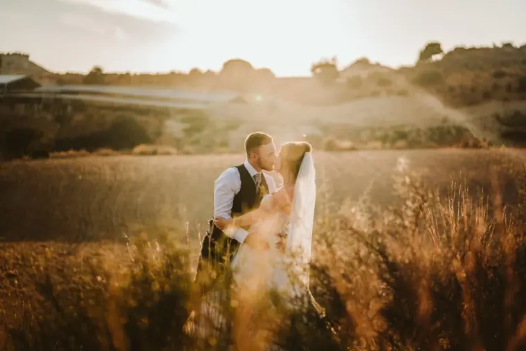 Couple kissing in a sunlit field at sunset with soft haze