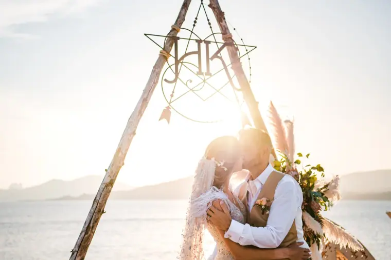 Sunlit kiss beneath the monogrammed tipi arch by the sea