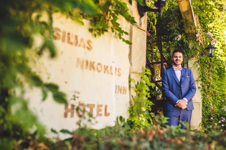 Groom standing beside the weathered Vasilias Nikoklis Inn Hotel sign