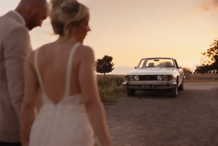 Couple walking towards the white convertible at sunset