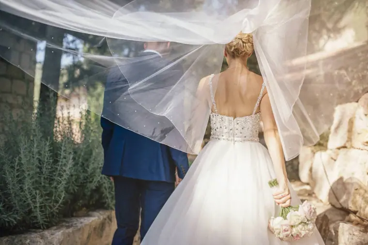 Groom lifting the bride's veil as it catches the breeze beside lavender