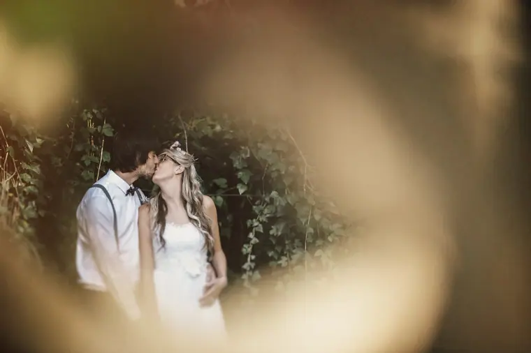 Bride and groom kissing in the garden, framed by blurred foliage