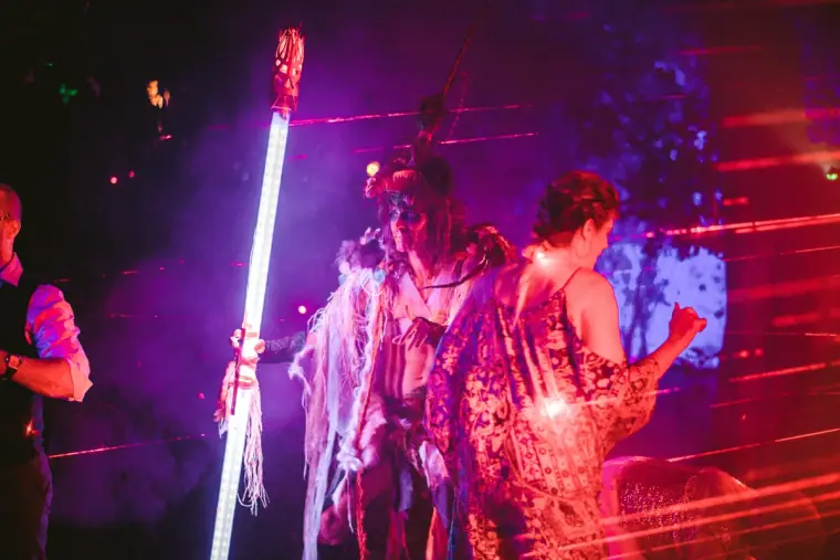 Dancers in fringed costumes performing with a glowing light wand under red lights