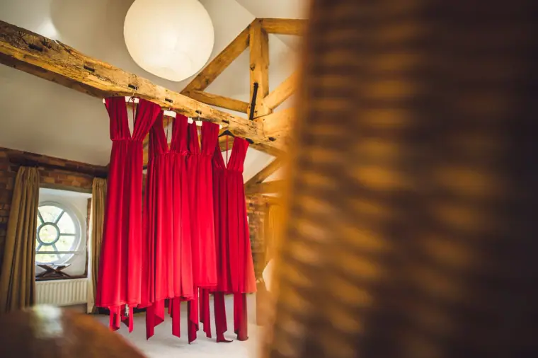 Red bridesmaid dresses hanging from an oak beam in the bridal suite