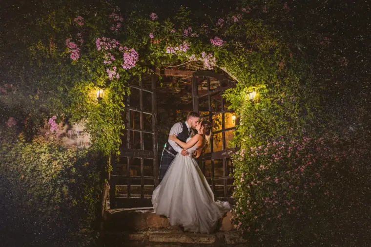 Couple embracing in a lit doorway framed by flowering vines at night