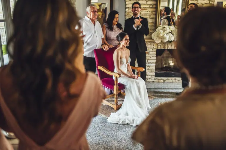 Ruby seated in her gown as family gather around during the bride's dressing