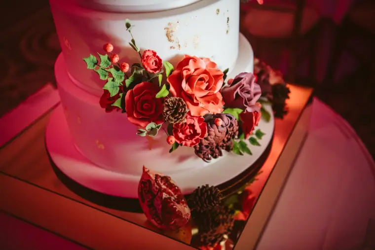 White tiered wedding cake decorated with red sugar roses under pink light