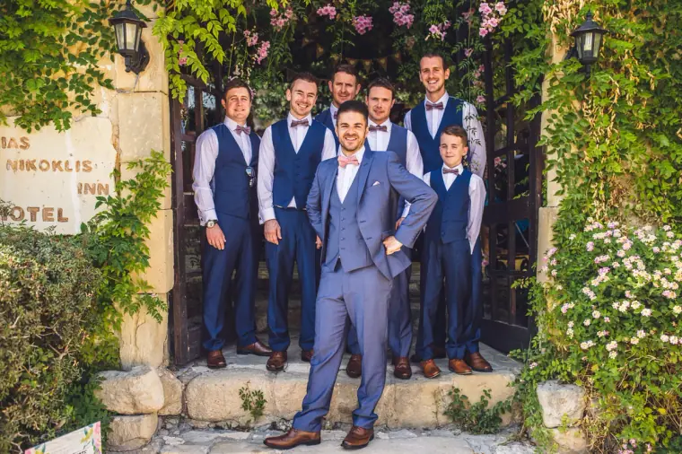 Groom and groomsmen in blue suits posing in the stone entrance of Vasilias Nikoklis Inn