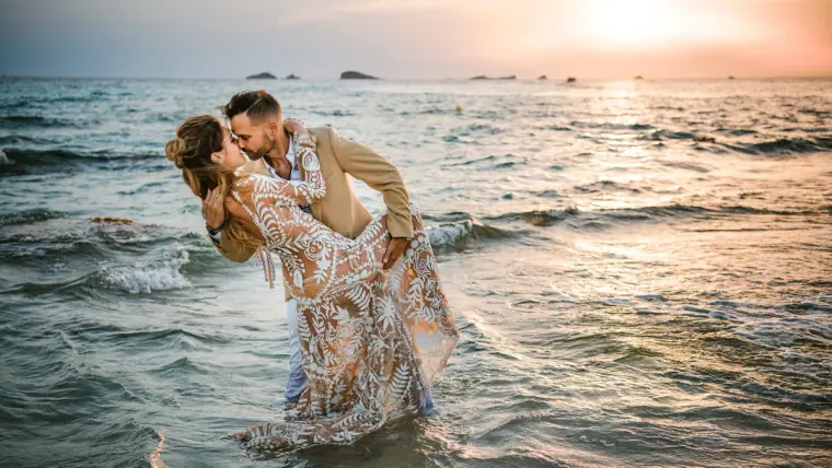 Groom dipping the bride for a kiss in the shallow sea at sunset