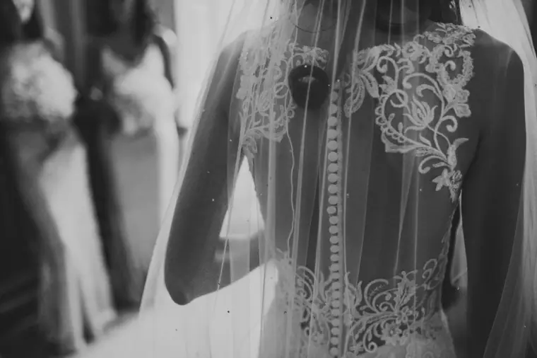 Black-and-white close-up of the lace back, buttons and veil of the bride's dress