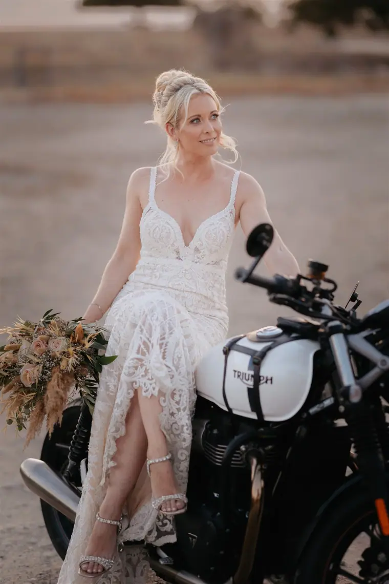 Bride sitting on a black motorbike holding her bouquet