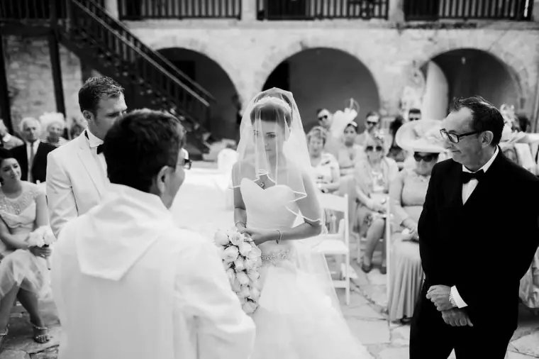 Black-and-white shot of the father bringing the veiled bride to the groom and priest