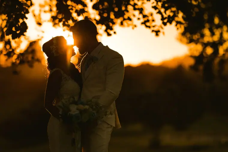 Backlit couple embracing beneath trees with the sun glowing between them