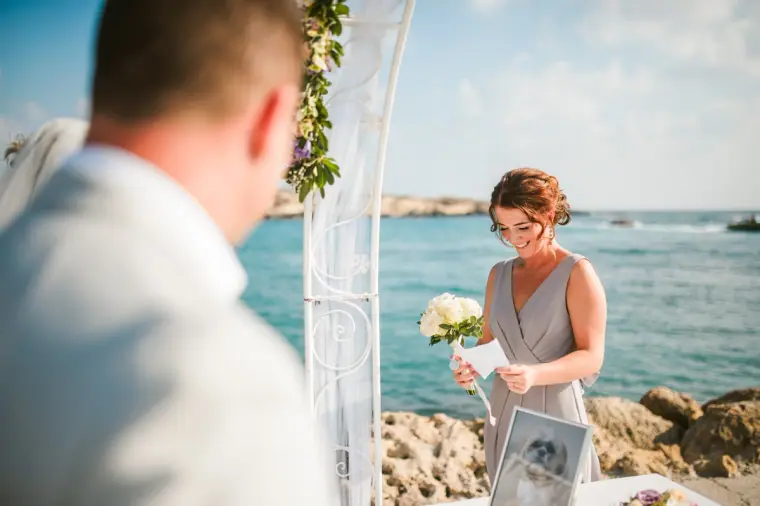 Bridesmaid giving a reading beside the arch with turquoise sea behind her