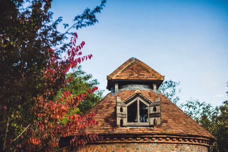 Tiled roof and lantern of the brick dovecote against a blue sky, Wasing Park