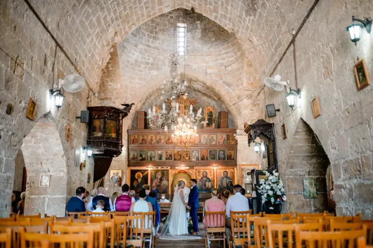 Wide view of the ceremony under the stone vaults and chandeliers of Ayia Kyriaki