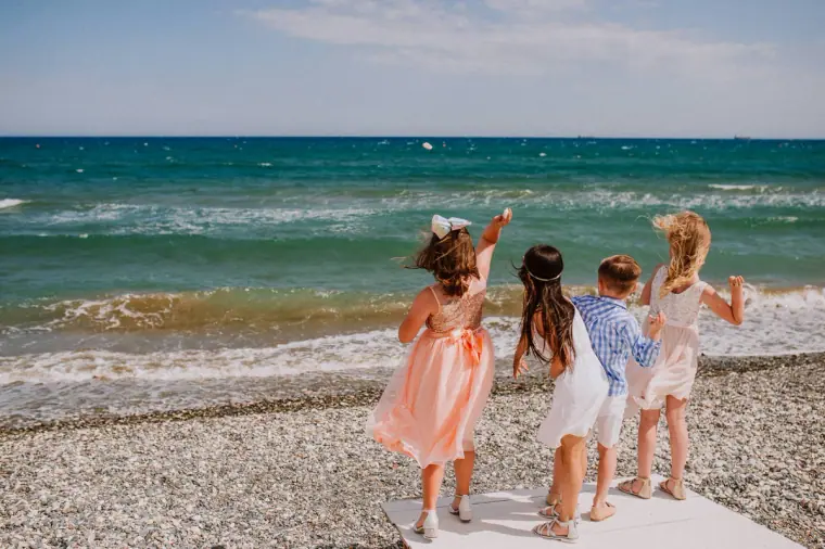 Flower girls and a pageboy waving at the sea on the shingle beach