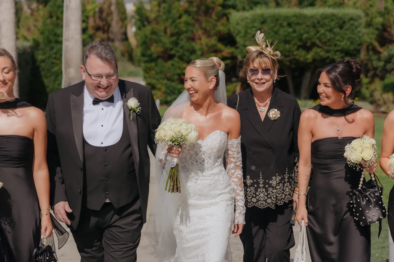Bride walking towards the ceremony with family and bridesmaids, all smiling
