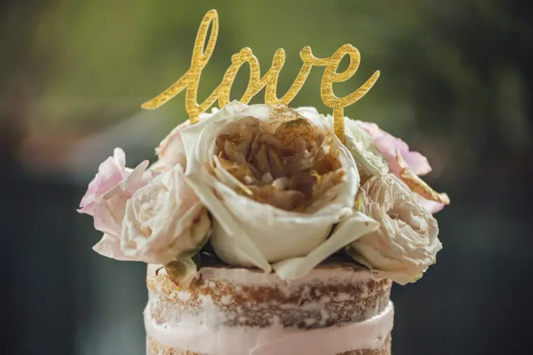 Gold glitter "love" topper on a semi-naked cake with ivory garden roses