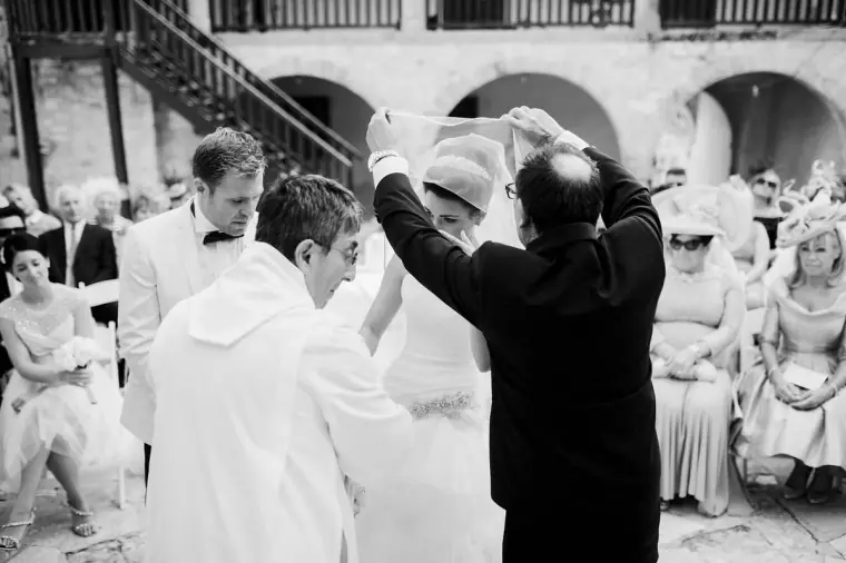 Black-and-white shot of the father lifting the bride's veil at the altar
