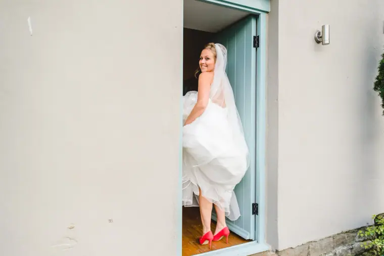 Bride lifting her skirt to reveal red shoes as she steps through a doorway