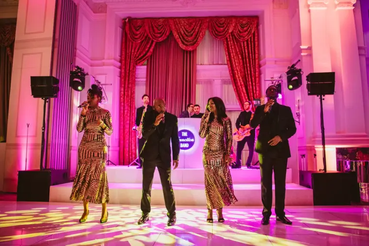 Live band with singers on stage under pink and purple lights and red curtains