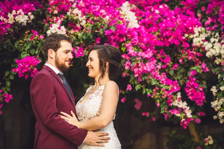 Madeliene and Itai smiling at each other in front of vivid pink bougainvillea