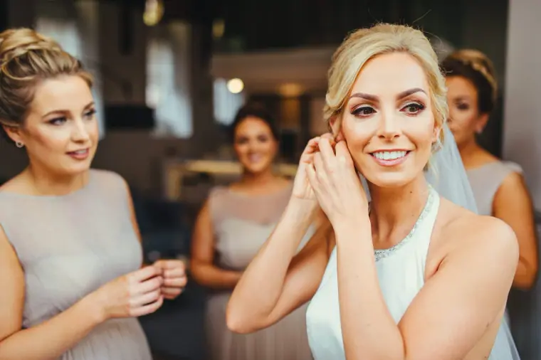 Leonnie putting on her earrings as bridesmaids in grey look on