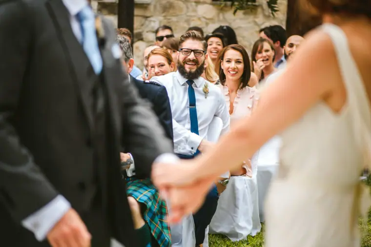 Bride's father handing her to the groom as guests look on smiling