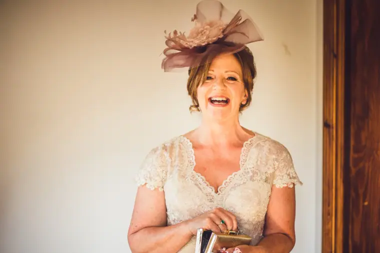 Guest in a lace dress and pink fascinator laughing in the bridal suite