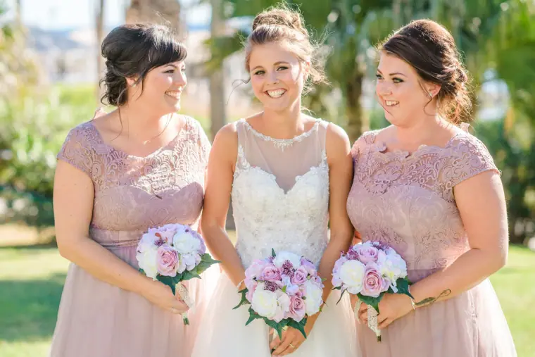 Bride laughing with two bridesmaids in blush lace holding pink bouquets